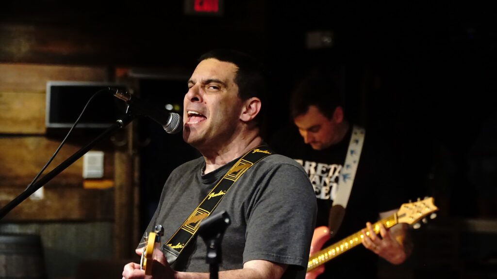 Mike singing at a microphone and looking into the camera to his left