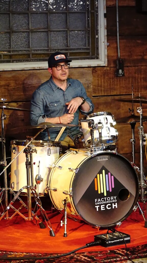 Picture of Jeff sitting behind drum kit holding drumsticks